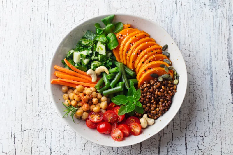 healthy vegetarian salad lentil, chickpea, carrot, pumpkin, tomatoes, cucumber wooden background top view