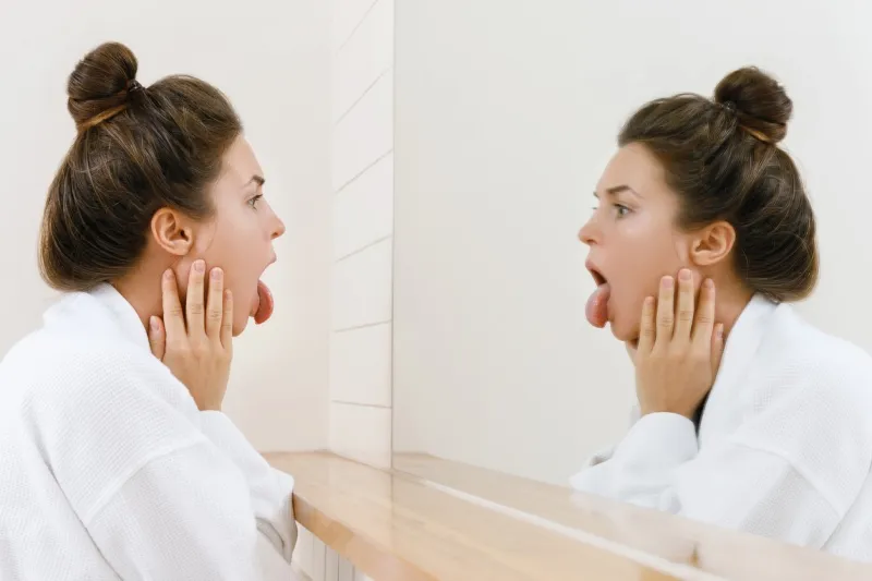 young woman is looking on her tongue in the mirror