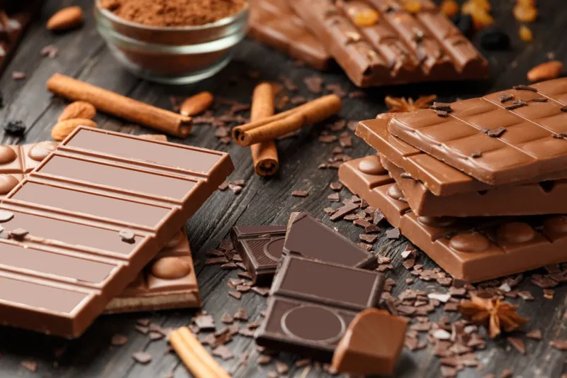 whole and broken chocolate, chocolate bars, candies, chocolate chips on a dark wooden background