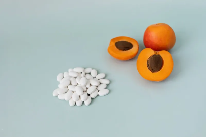 flat layout of a handful of white pills vitamin b17 or amygdalin lays on blue background, some apricots (peaches) are beside cancer treatment, laetrile horizontal plane, copy space