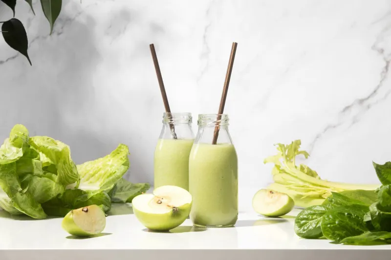 green detox smoothies in two bottles standing on a white table, front view composition, healthy lifestyle concept