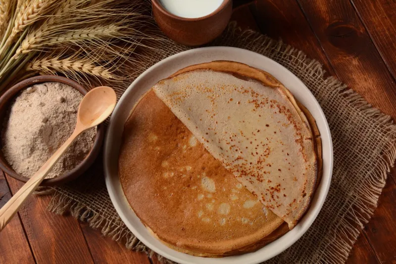 a traditional french savory buckwheat galettes bretonnes pancakes on a table with flour, wheat plant and milk