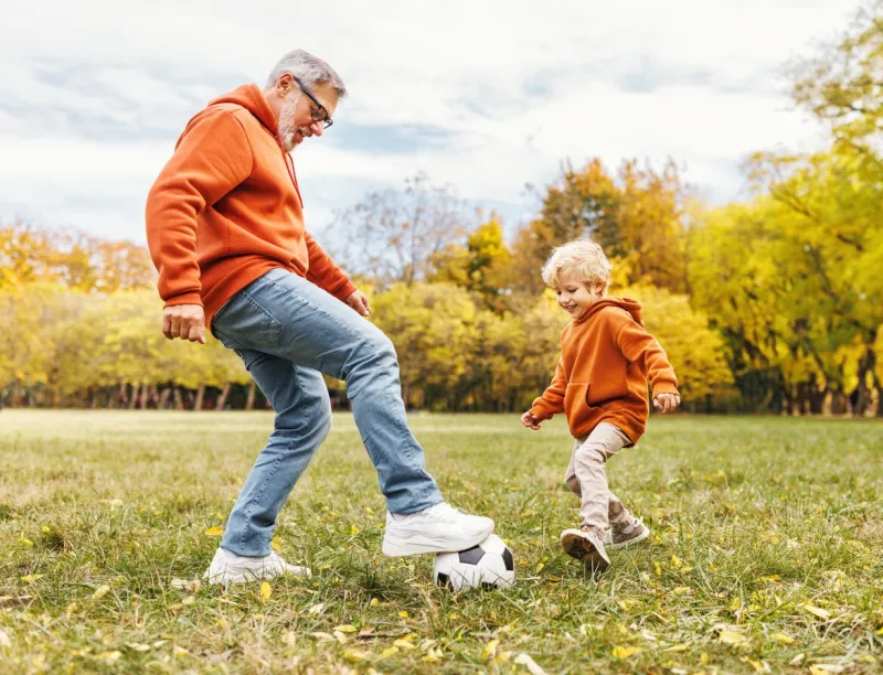 happy family grandfather and grandson play football on lawn in the park