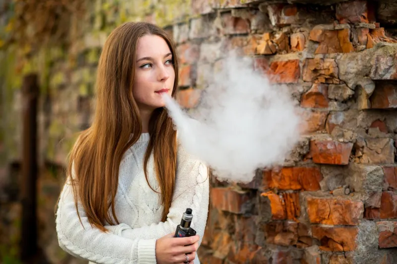 vaping teenager young pretty white caucasian teenage girl with problem skin smoking an electronic cigarette the ruined brick wall on the street in the autumn bad habit vape activity