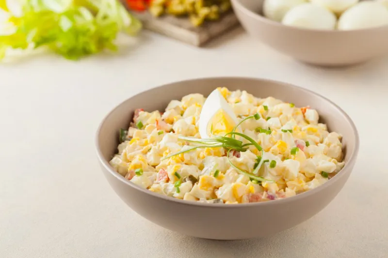 a light egg salad with celery, gherkin, pepper and mayonnaise served in a bowl on a light background front view