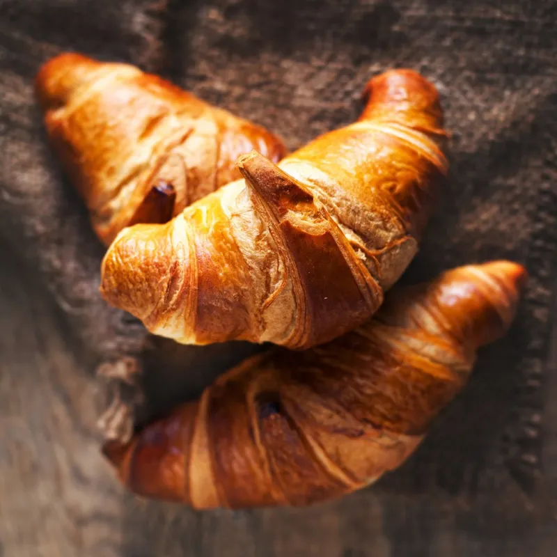 golden fresh croissants on old wooden background close up with copyspace, rustic concept