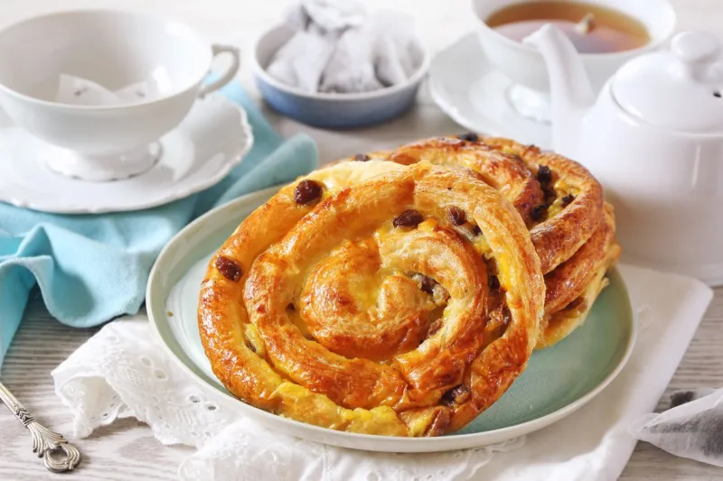 french roll raisin buns, teapot and cup of tea bag on light background