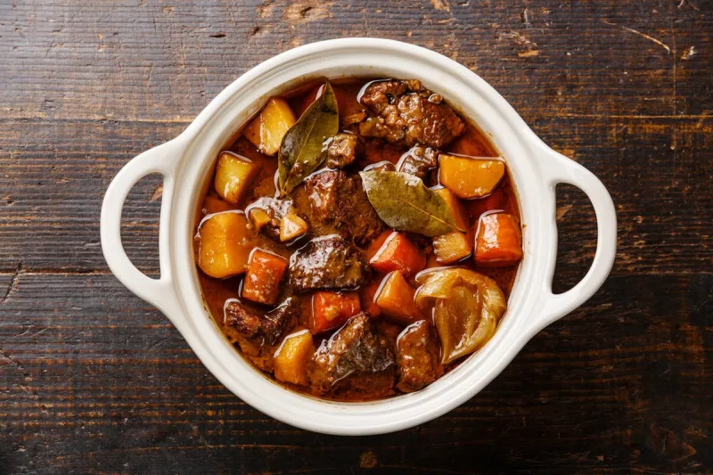 beef meat stewed with potatoes, carrots and spices in ceramic pot on wooden background