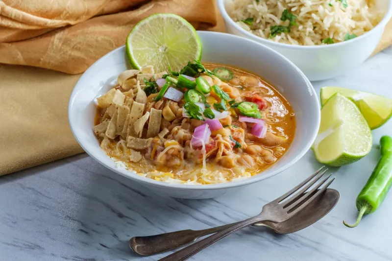 white navy bean chicken chili with tortilla strips lime cilantro and shredded cheese garnish