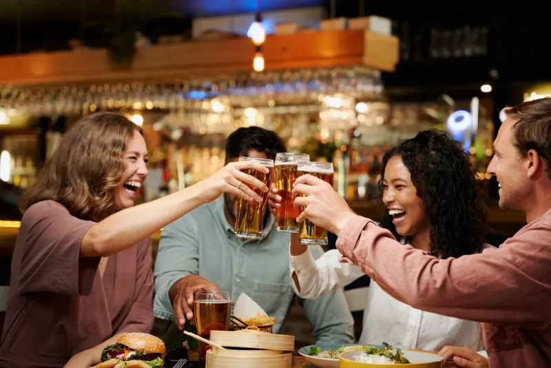young multiracial group of friends wearing casual clothing celebrating with drinks and dinner at restaurant