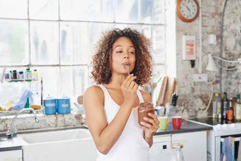 shot of a young woman eating a chocolate spread from the jar