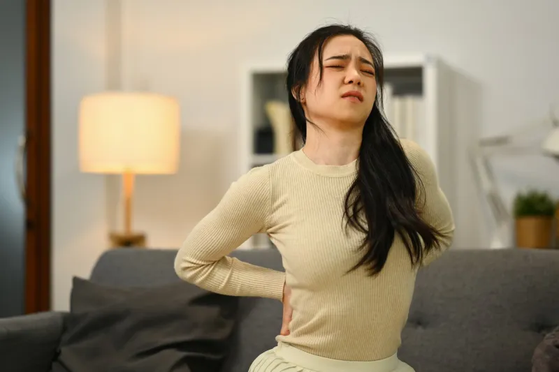 unhappy young woman suffering from lower lumbar backache spine health problems and health care concept