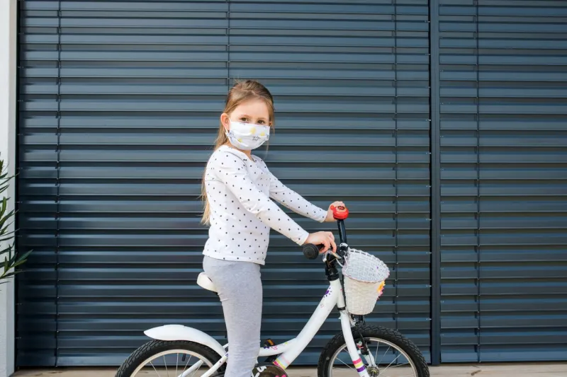 small girl with bicycle and face mask outdoors at home corona virus and quarantine concept