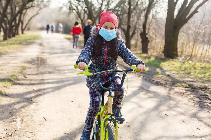 7 years old happy little girl child ride bicycle in the park at home and wearing protection mask for protect pm25 and coronavirus covid-19 pandemic virus symptomssport exercise for health