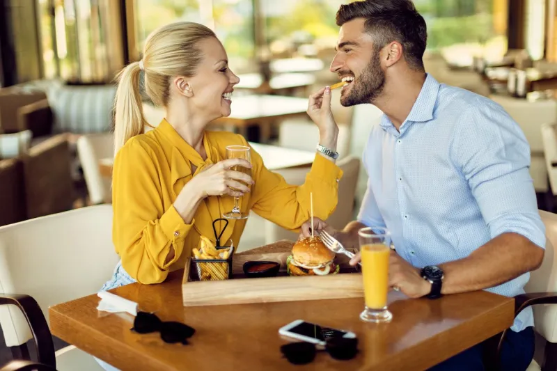 happy couple having fun during lunch time in a restaurant woman is feeding man with french fries