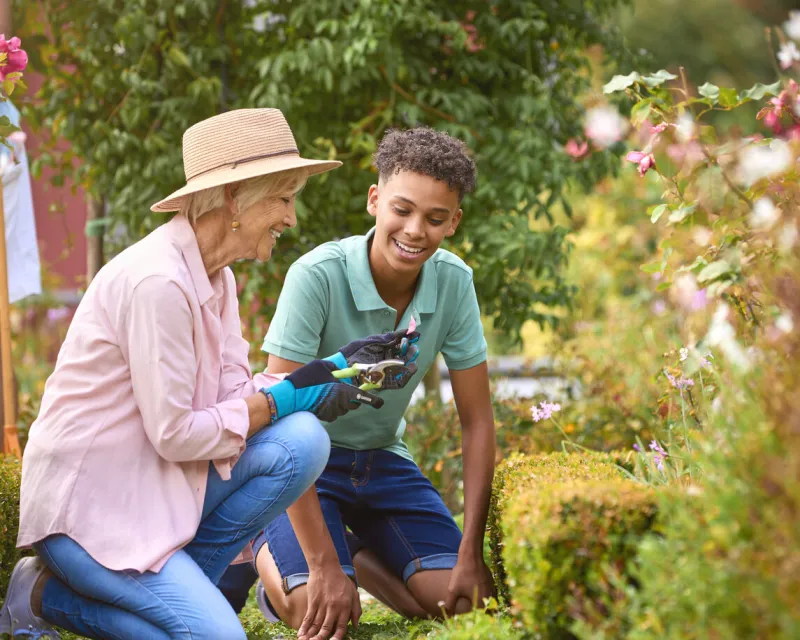 teenage grandson helping grandmother with gardening at home learning about plants and nature
