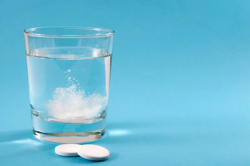 recovering from a hangover and nursing a headache with aspirin concept with effervescent drink tablet dissolving in water with two tablets outside the glass isolated on blue background with copy space