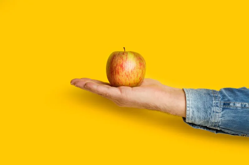 man holding a red apple in his hand on a yellow background