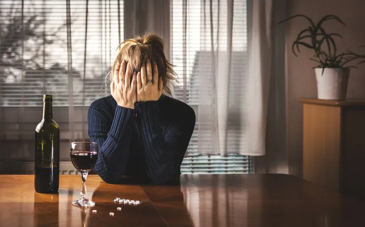 depressed woman is drinking red wine and taking pills at home alone