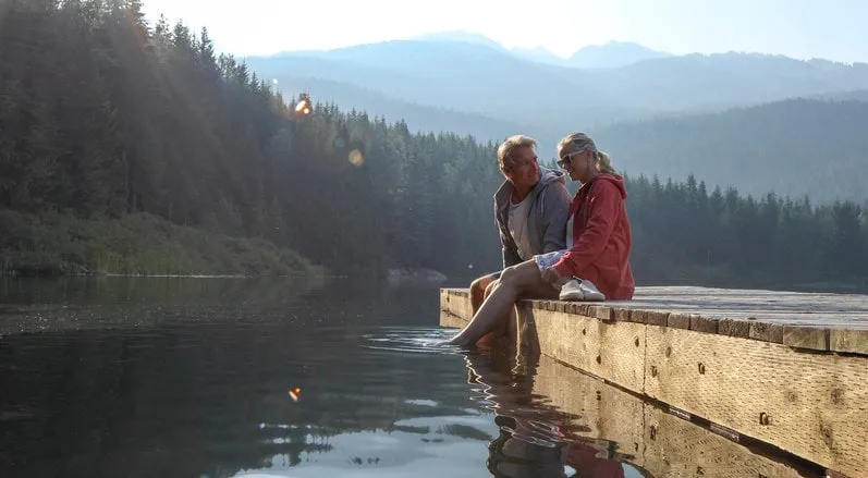 mature couple relax on wooden pier, looks out across lake