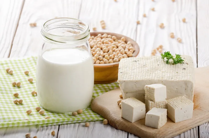 non-dairy alternatives soy milk or yogurt in mason jar and tofu on white wooden table with soybeans in bowl aside