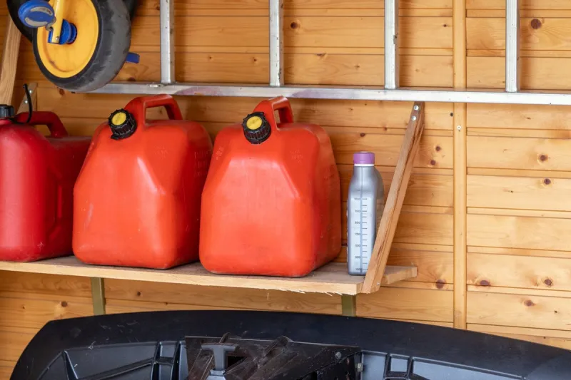 garage corner with three red plastic fuel cans , staircase and snow plough for atv with wooden wall on background petrol gas containers reserves storage at vehicle home garage