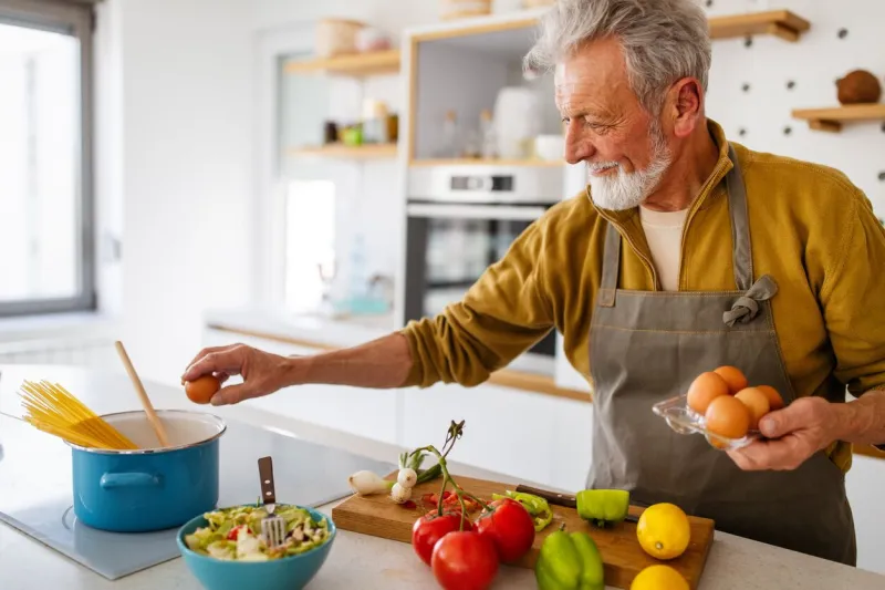 happy retired senior man cooking in kitchen retirement, hobby people concept