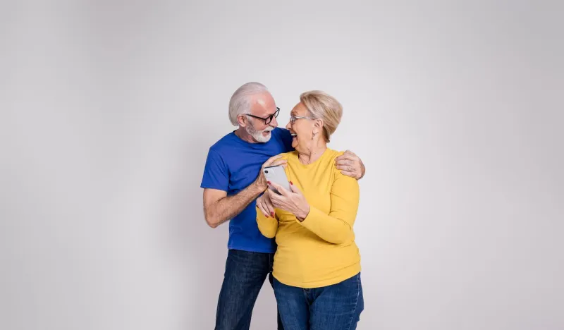 mature couple with smart phones looking at each other and laughing ecstatically on white background