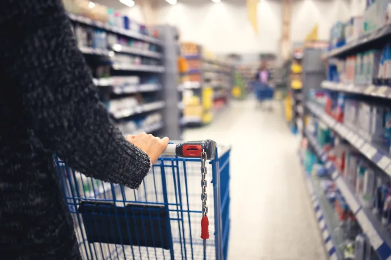 a women walks with a shopping basket in a store hand and part of the basket in focus, blurred background