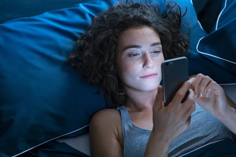 girl awake in bed using cellphone at night