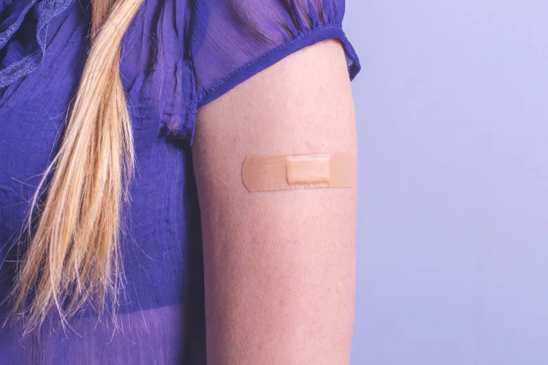 female arm with adhesive bandage on blue background with copy space