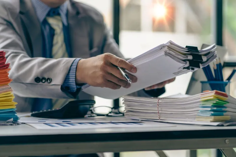 businessman working in finance with pile of unfinished papers on the desk business paper pile