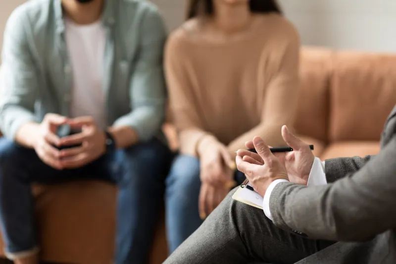 help concept closeup cropped view of male counselor therapist or consultant in suit talking with couple sitting in office, giving professional advice selective focus on hands with clipboard and pen