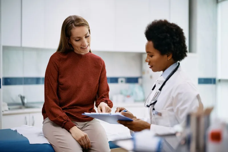 african american doctor and her female patient analyzing medical report after examination in the hospital focus is on female patient