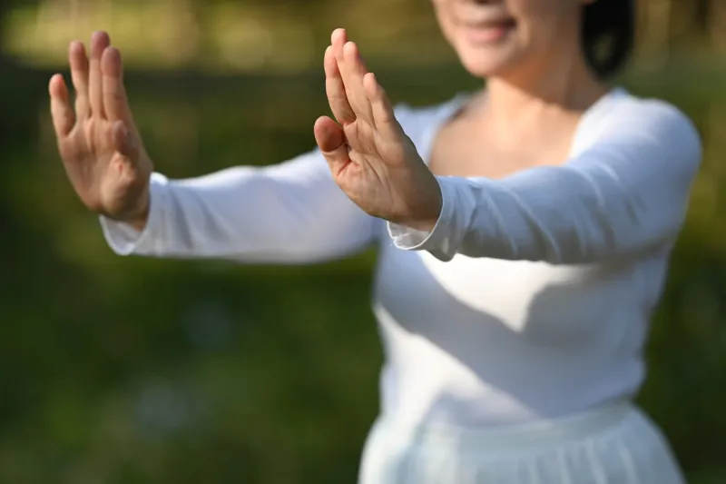 smiling senior woman in white clothing practicing tai chi in the park health care concept