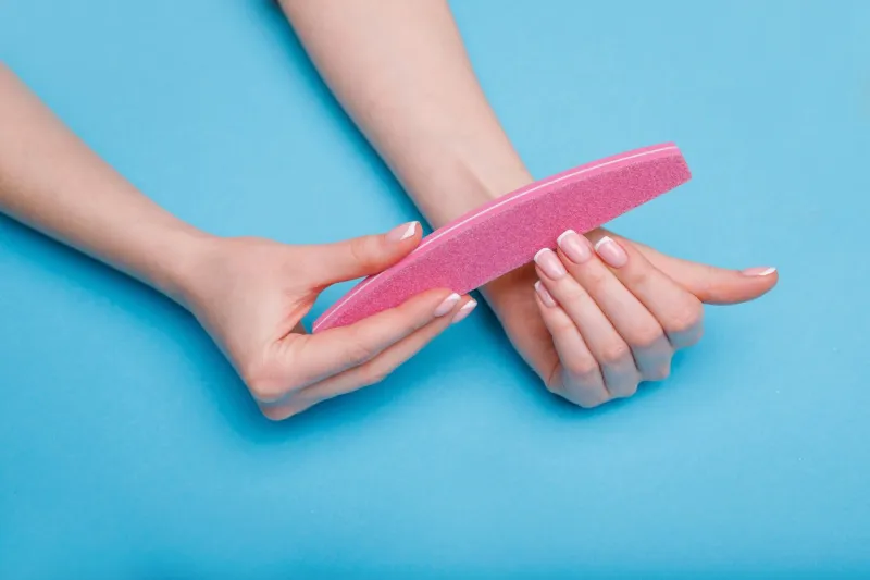beautiful female hands with stylish nail manicure gel polish on blue background top view of manicure equipment woman files her nails