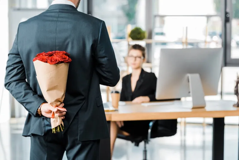cropped image of businessman hiding bouquet of roses behind back to surprise businesswoman in office