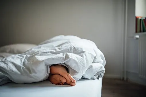 low section of young woman sleeping in bed female's bare feet under blanket in bedroom she is resting at home