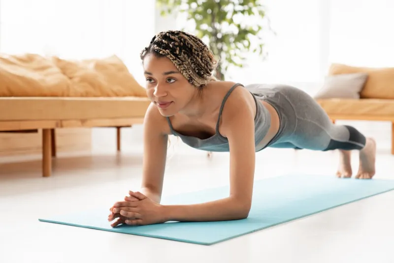 fit sporty african-american young woman standing in plank position in fitness clothes at home cheerful african woman stretching up, doing home workout