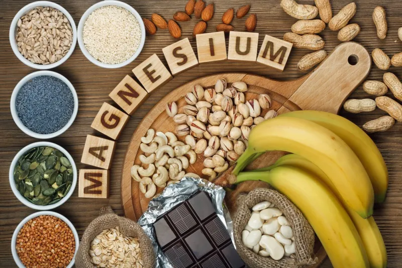 products containing magnesium  bananas, pumpkin seeds, blue poppy seed, cashew nuts, beans, almonds, sunflower seeds, oatmeal, buckwheat, peanuts, pistachios, dark chocolate and sesame seeds on wooden table