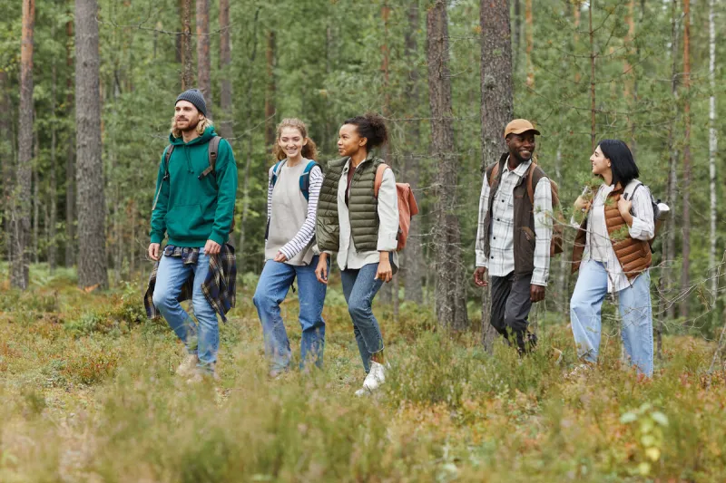 diverse group of young people walking in forest with backpacks while exploring hiking trails, copy space