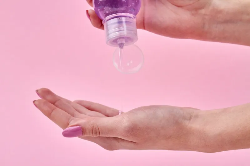 woman's squeezing shampoo on her palm close up transparent liquid soap flow from a bottle isolated on pink background