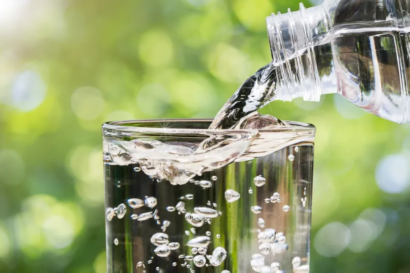 close up of water flowing from drinking water bottle into glass on blurred green nature bokeh background, healthy drinking clean water concept