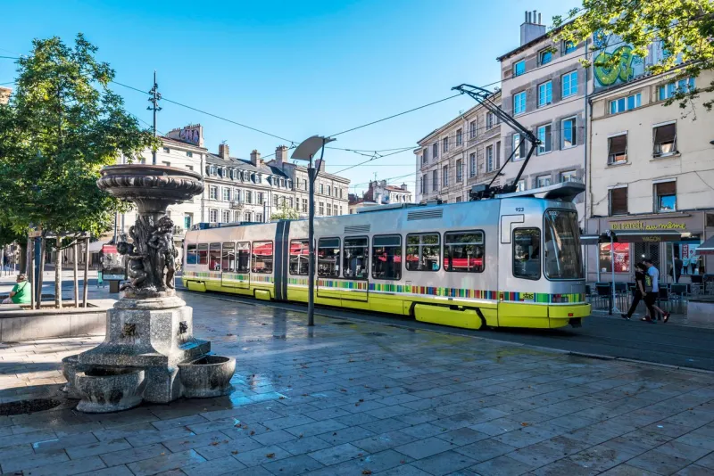 saint-etienne, france - july 29, 2019 street view in saint etienne downtown the tramway passing along the square place du peuple the statue with fountain is at foreground