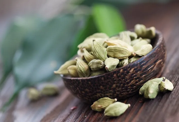 angled view of cardamom spices in wooden bowl