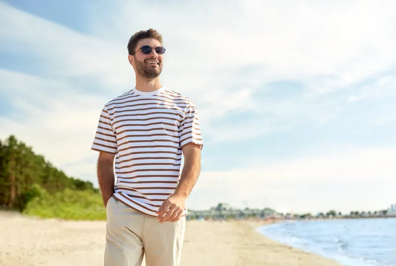 summer holidays and people concept - portrait of young man in sunglasses walking along beach in tallinn, estonia
