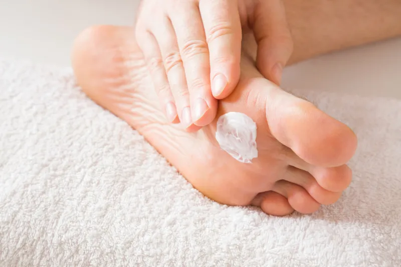 groomed, young man's hand applying feet moisturizing cream barefoot on the white towel cares about clean and soft legs skin healthcare concept