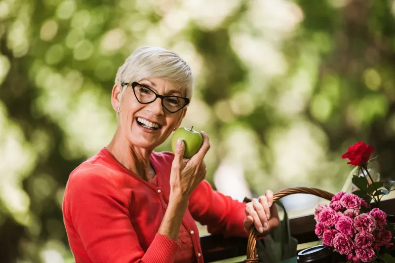 healthy looking senior woman with grey hair holding apple outside in the park