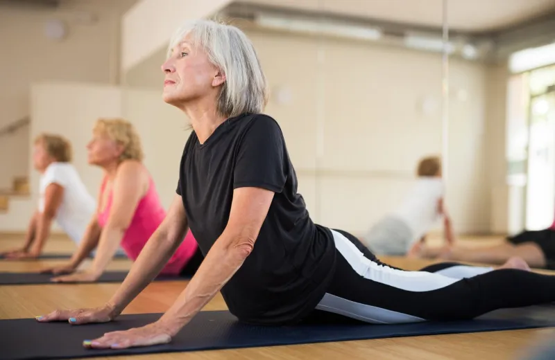 senior women practicing cobra pose during group yoga training