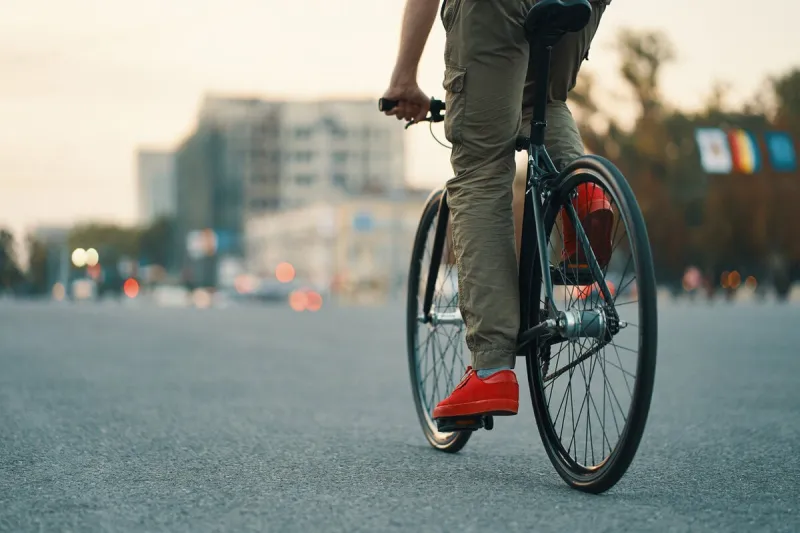 closeup of casual man legs riding classic bike on city gray road wearing red sneakers and comfy pants copy space
